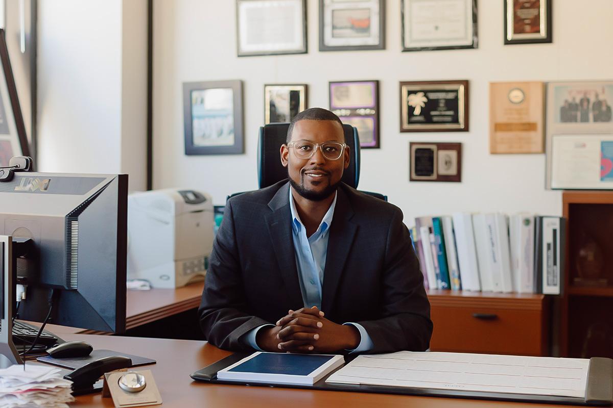 a faculty member sitting behind a desk smiling